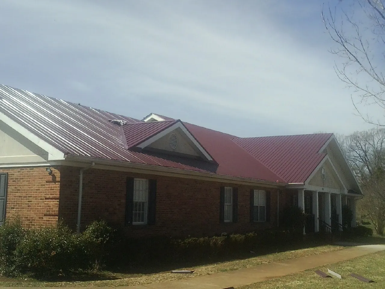 Red metal roof with gabled entries on a long brick building, from a Hail Damage Roof Repair job in Port Crane