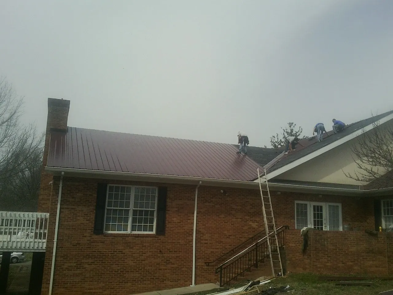 Crew setting red metal roofing panels on a brick home in Port Crane