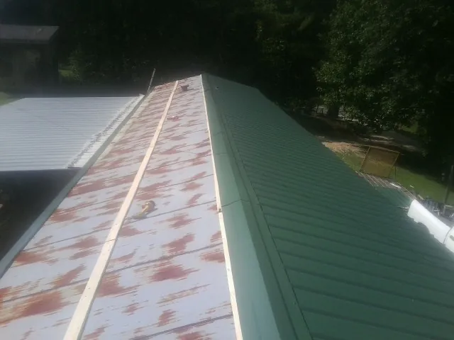 Old rusted panels beside newly installed green metal roofing — Wind Damage Roof Repair by Roofing Brothers in Port Crane