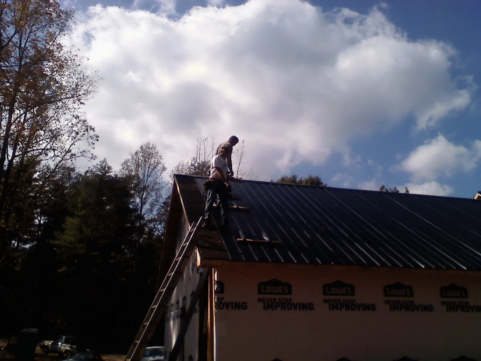Roofer fastening dark metal panels high against a cloudy sky, from a Roof Inspection job in Port Crane