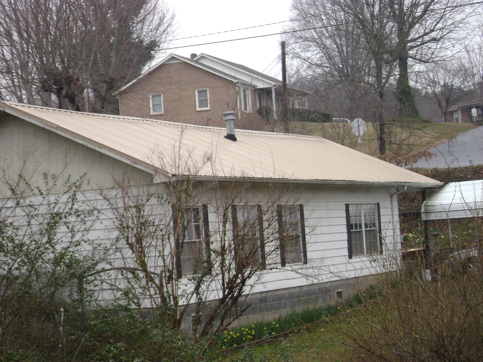 Tan metal roof on a white sided house set into a hillside — Commercial Roofing by Roofing Brothers in Port Crane