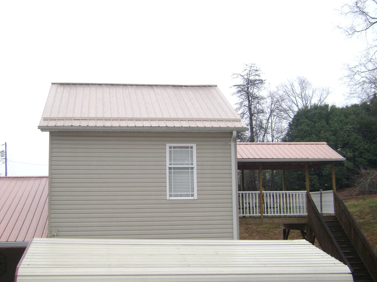 Tan metal roofs on a two story addition and attached porch, from a Roof Replacement job in Port Crane
